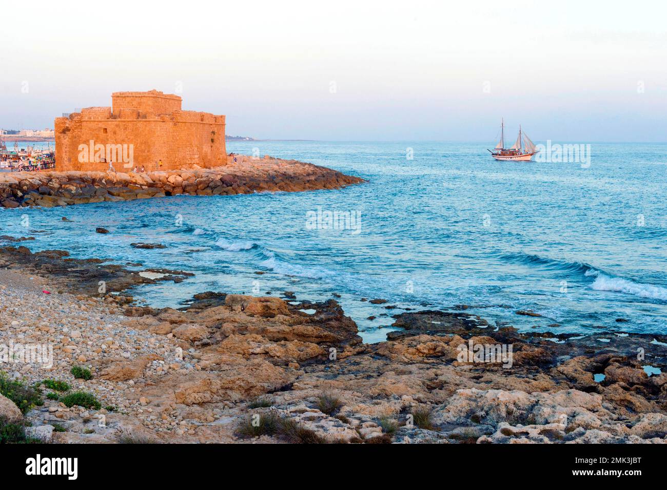 Die mittelalterliche Festung am Hafen ist eines der wichtigsten Wahrzeichen von Pafos. Ein Segelboot fährt im Abendlicht für eine hin- und Rückfahrt ab. Stockfoto