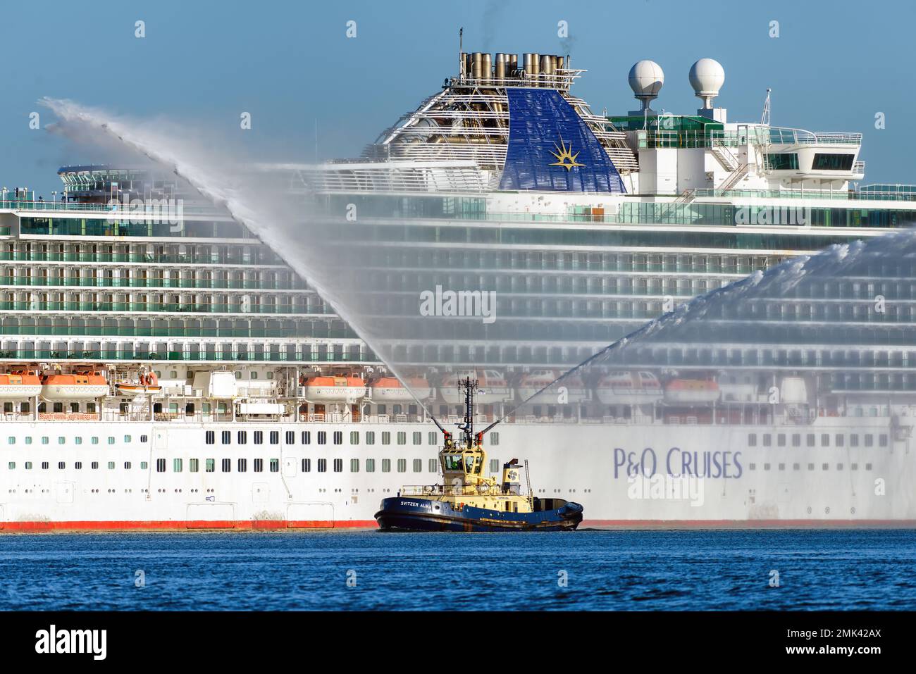 Der Svitzer Towage Tug Svitzer Alma bietet einen Wassersalut für das P&O Kreuzfahrtschiff Azura im Hafen von Southampton. Stockfoto