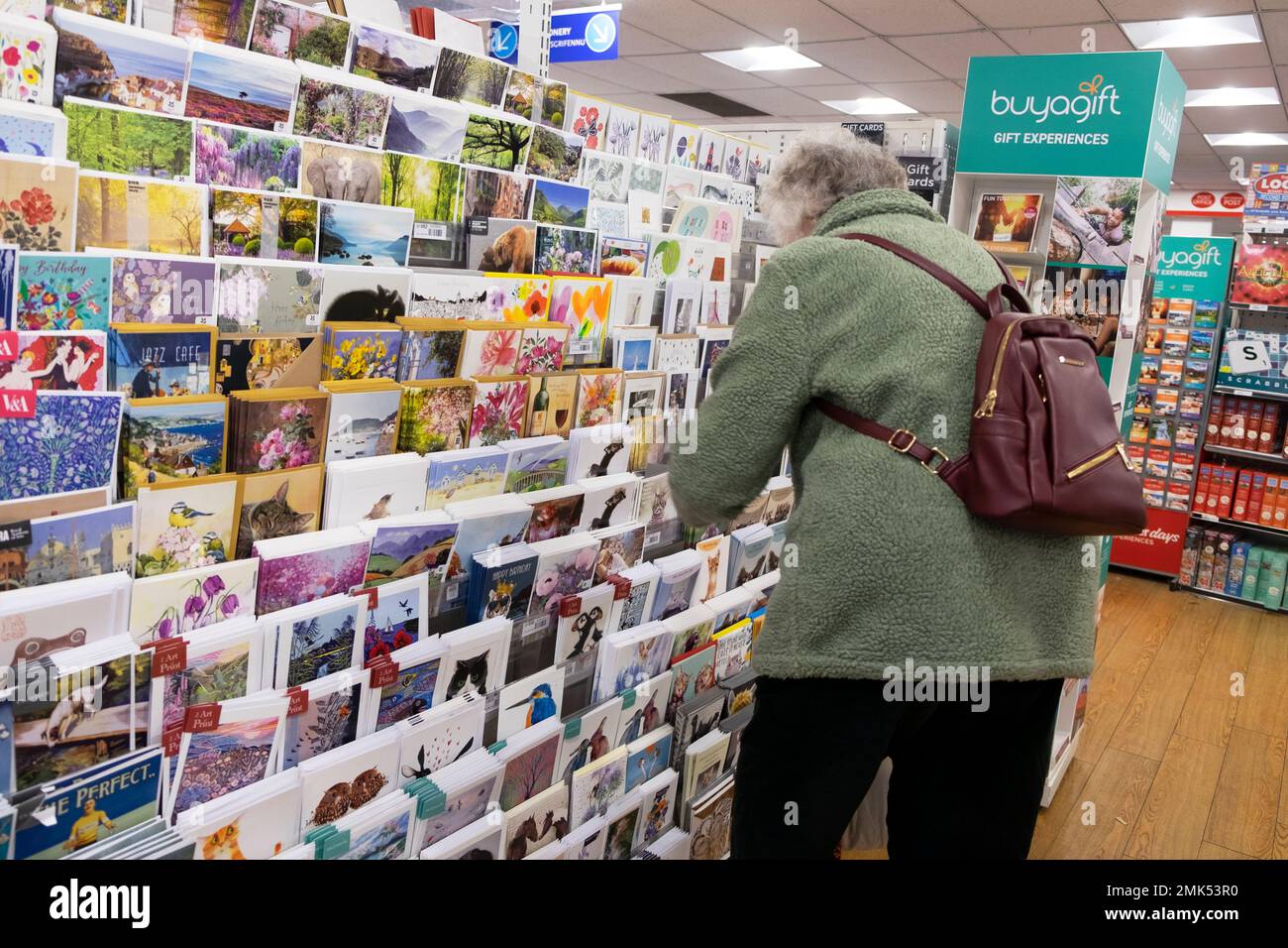 Rückblick ältere Seniorin mit Rucksack, die sich bückt, um Grußkarten zum Verkauf in Briefpapier W.H. anzusehen Smith Store, 28. Januar 2023, Großbritannien Stockfoto