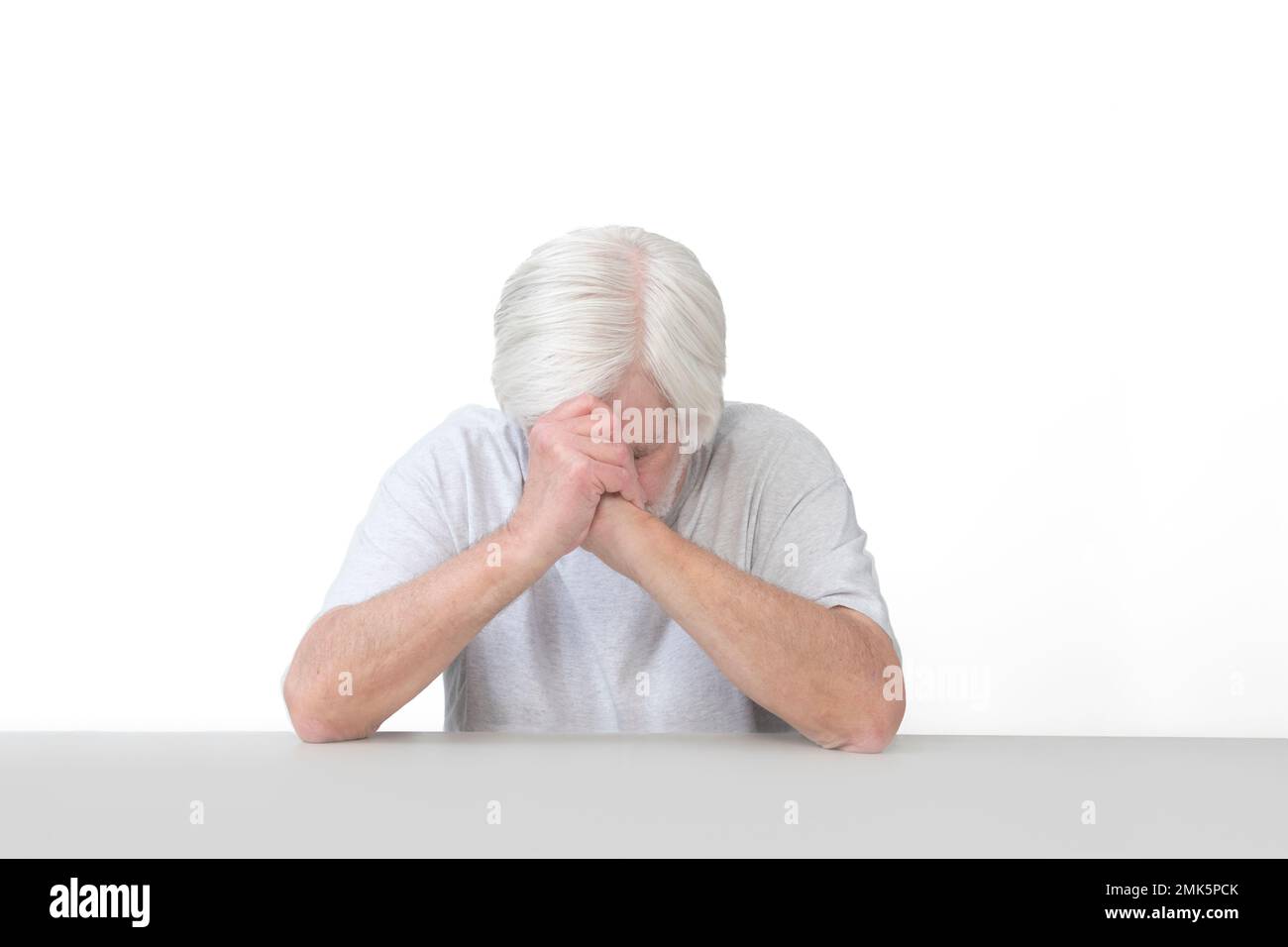 Horizontale Aufnahme eines alten Mannes, dessen Ellbogen sich auf einem Tischkopf verbeugt im Gebet. Isoliert auf weiß. Viel Platz zum Kopieren. Stockfoto