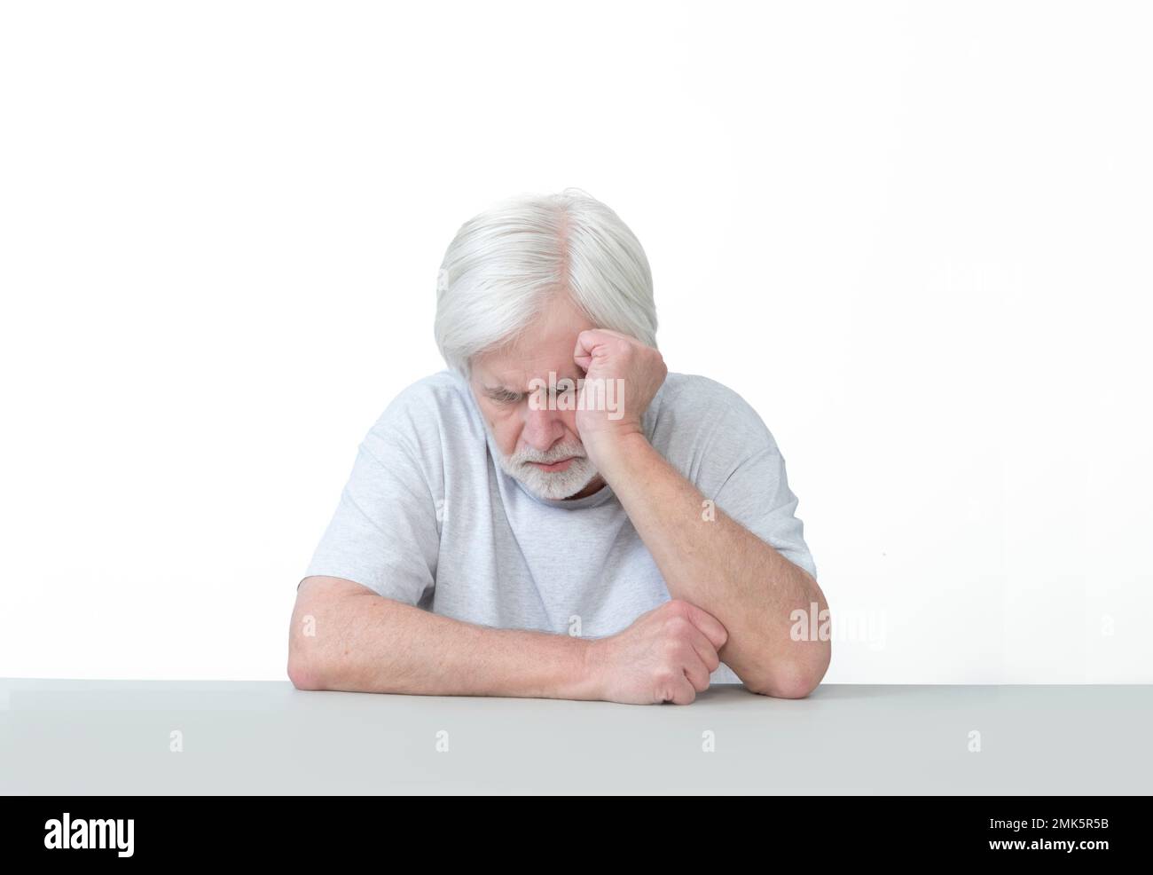 Horizontale Aufnahme eines müden alten Mannes, der an einem Tisch schläft und seinen Kopf an die Hand lehnt. Isoliert auf weiß. Viel Platz zum Kopieren. Stockfoto