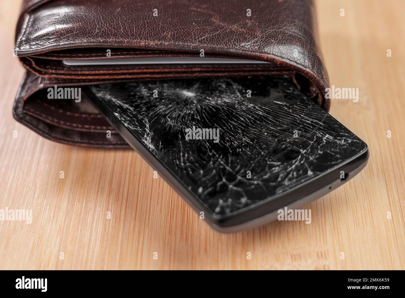 Ein kaputtes Handy mit einem zertrümmerten schwarzen Glasschirm in einer braunen Ledertasche. Konzeptionelle Ansicht Stockfoto