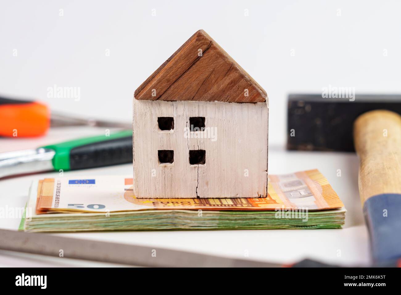 Holzriss-Hausmodell auf Geldbündel mit Werkzeugen. Das Konzept eines Finanzprojekts für die Renovierung und Umgestaltung eines Hauses Stockfoto