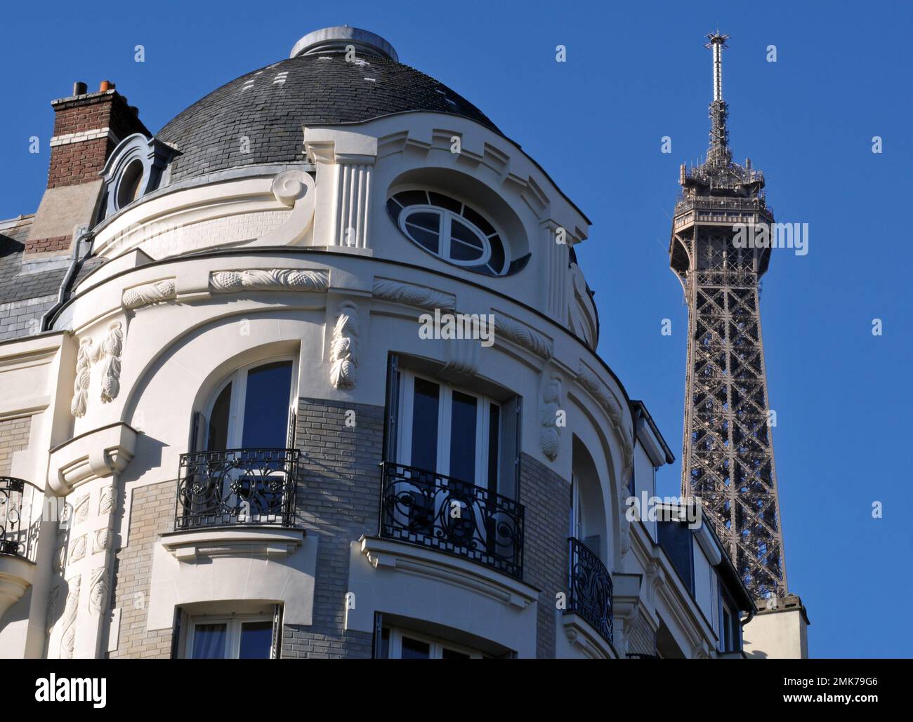 Der Gipfel des berühmten Eiffelturms erhebt sich hinter einem prunkvollen Wohngebäude in Paris. Stockfoto