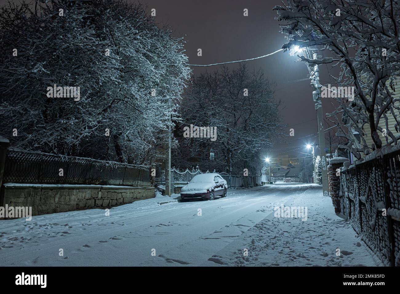 Auto auf einer verschneiten Straße in einer Kleinstadt bei Nacht. Stockfoto