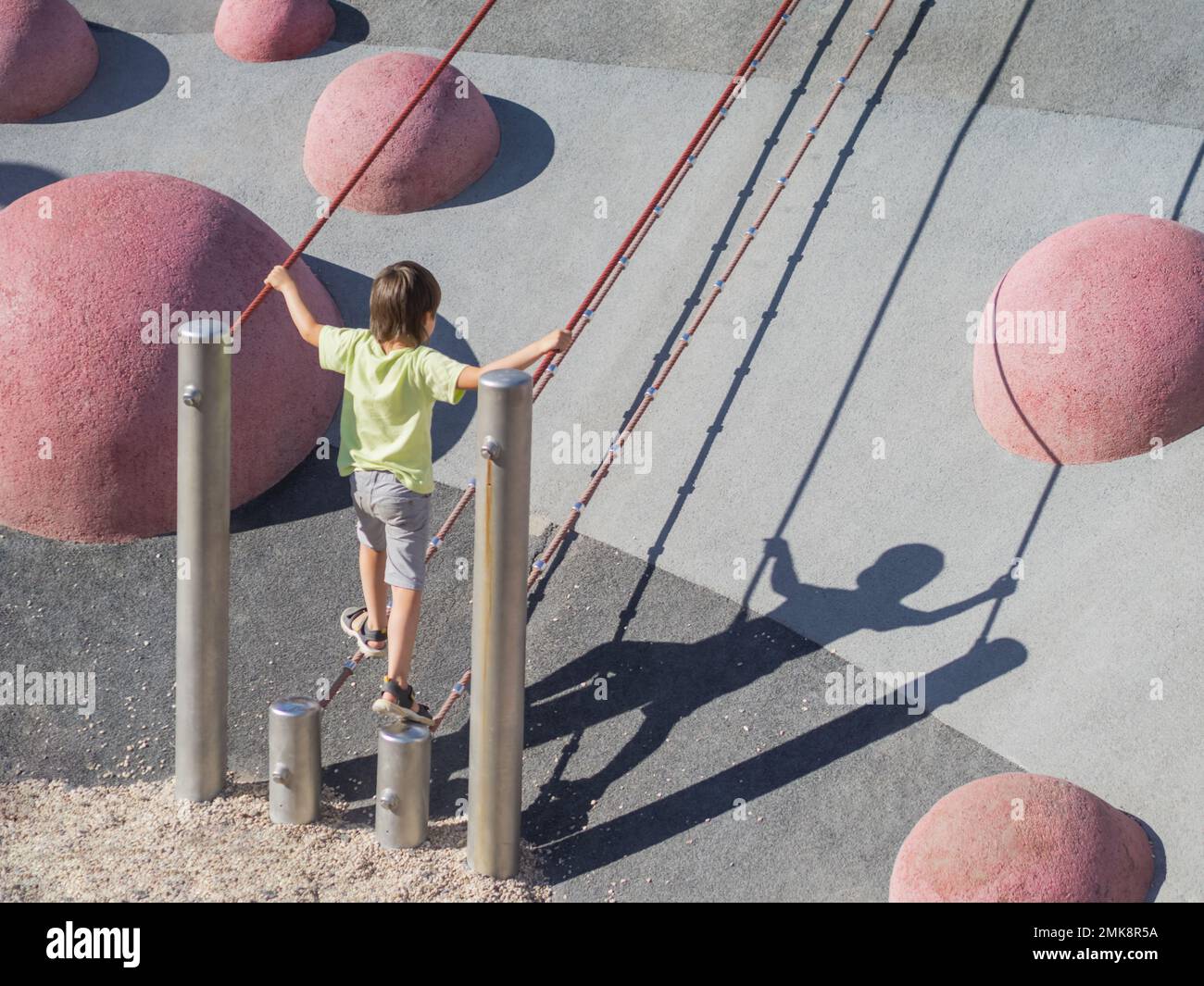 Der Junge klettert einen Betonhang auf dem modernen Kindersport- und Spielplatz hinauf. Das Kind überwindet die Angst und lernt neue Dinge. Aktive Freizeitaktivitäten im Freien. Stockfoto