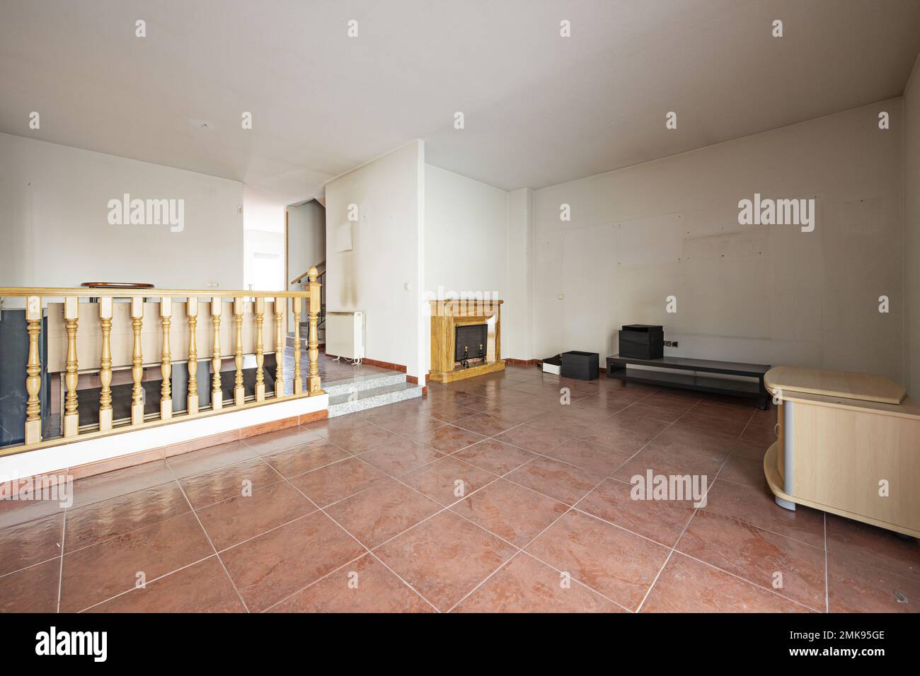 Wohnzimmer auf zwei Ebenen mit einem Holzgeländer und zwei Stufen mit roten Steinzeug-Böden eines Einfamilienhauses mit Kamin Stockfoto