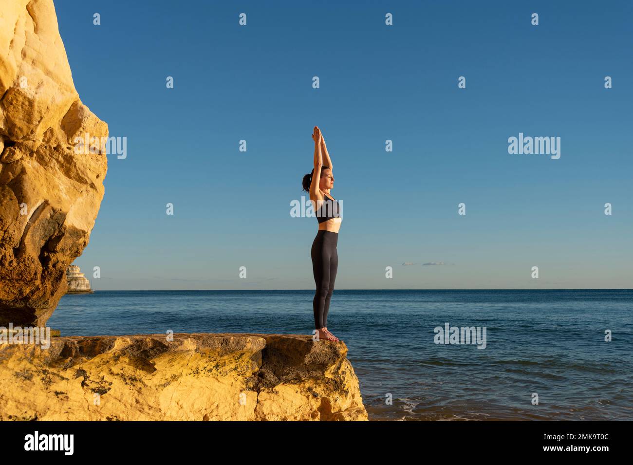 Fit, weiblich, die Yoga auf einem Felsen am Meer praktiziert. Stockfoto