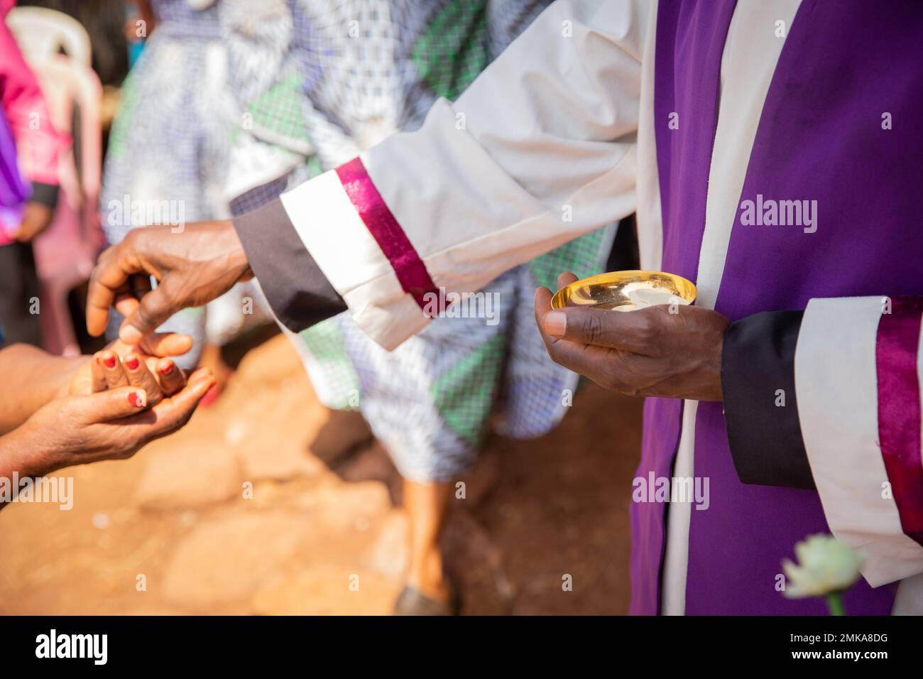 Ein afrikanischer Priester gibt einem Gläubigen sakramentales Brot, konzentriert sich auf die Hand mit sakramentalem Brot Stockfoto