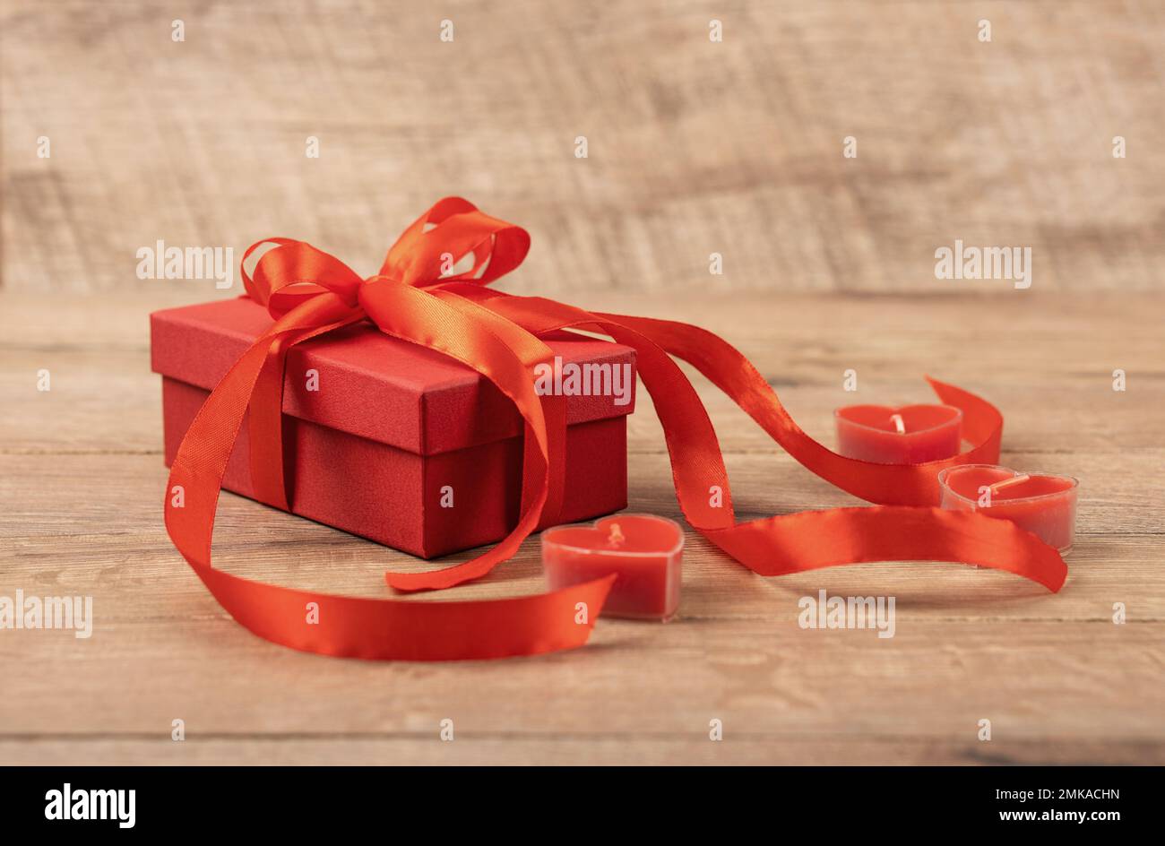 Grußkarte zum Valentinstag, Muttertag und Geburtstag. Rote Geschenkbox mit einer roten Schleife aus Satin und roten Kerzen in Herzform auf einem Stockfoto