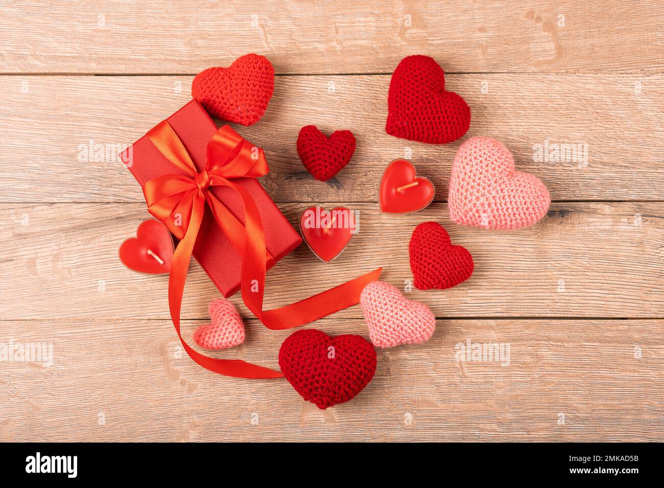 Rote Geschenkbox mit gestrickten roten Herzen und mit roten Kerzen in Herzform auf Holzhintergrund. Alles gute zum Valentinstag, Muttertag und bir Stockfoto
