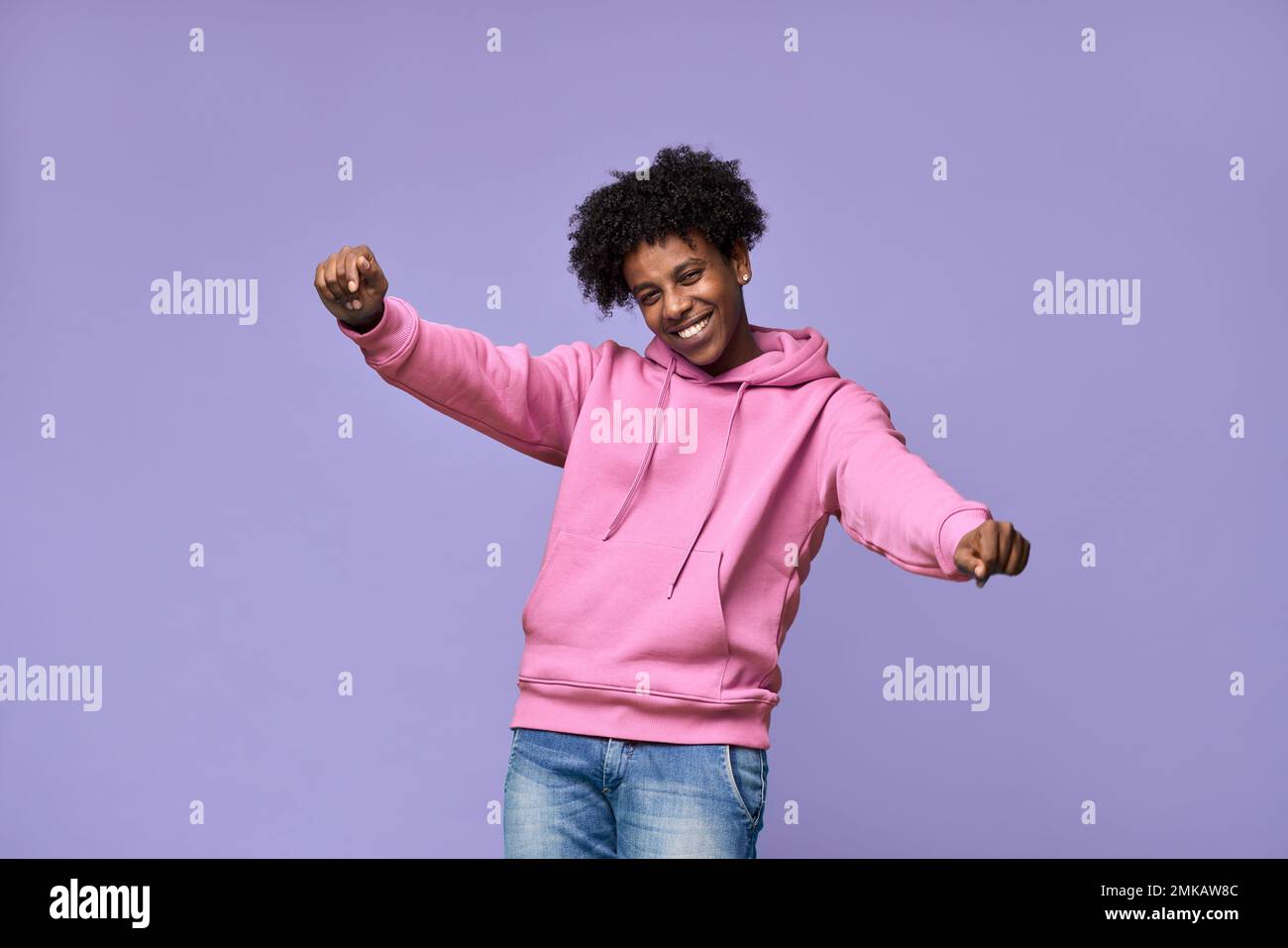 Flippiger afrikanischer Teenager mit pinkfarbenem Kapuzenpulli, der isoliert auf lila Hintergrund tanzt. Stockfoto