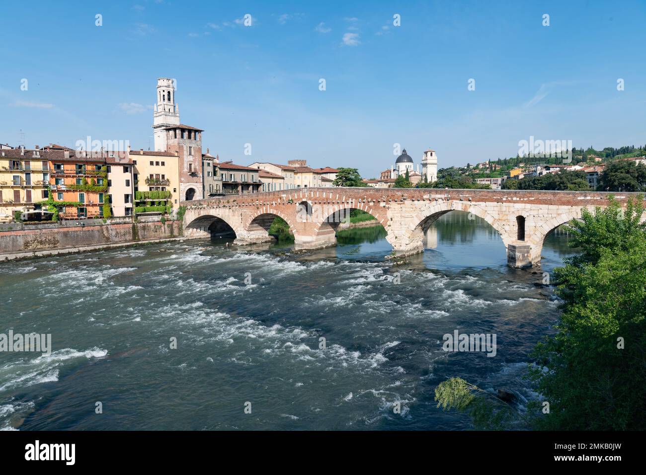 Schnell fließendes Wasser fließt unter den Bögen der Ponte Pietra Brücke, die die Fiume Adige in Verona, Italien, vor klarem blauen Himmel überspannt Stockfoto