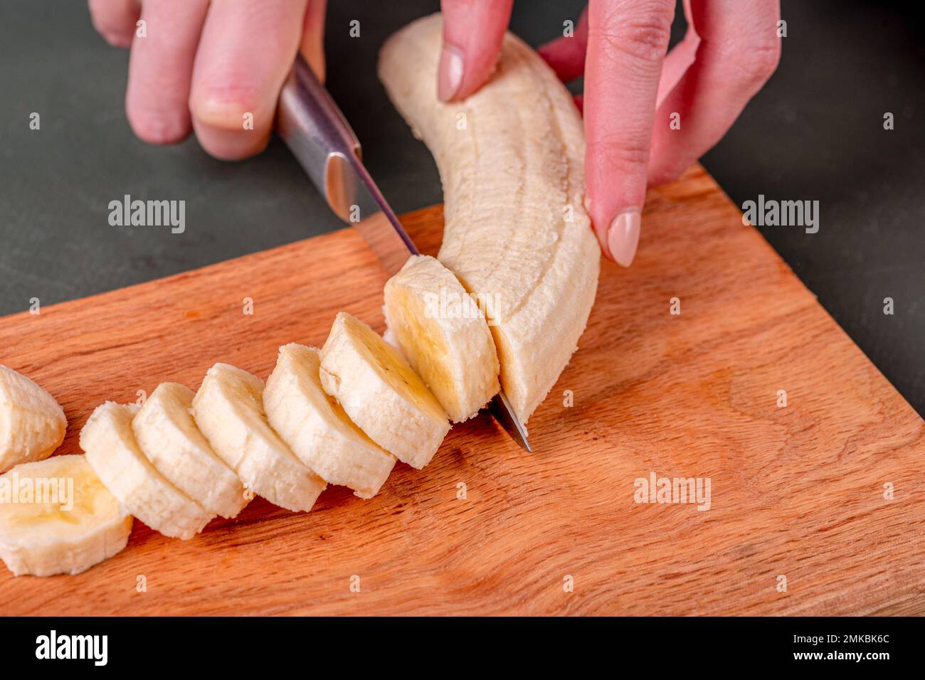 Frau schneidet Banane mit Messer auf Holzbrett in der Küche. Stockfoto