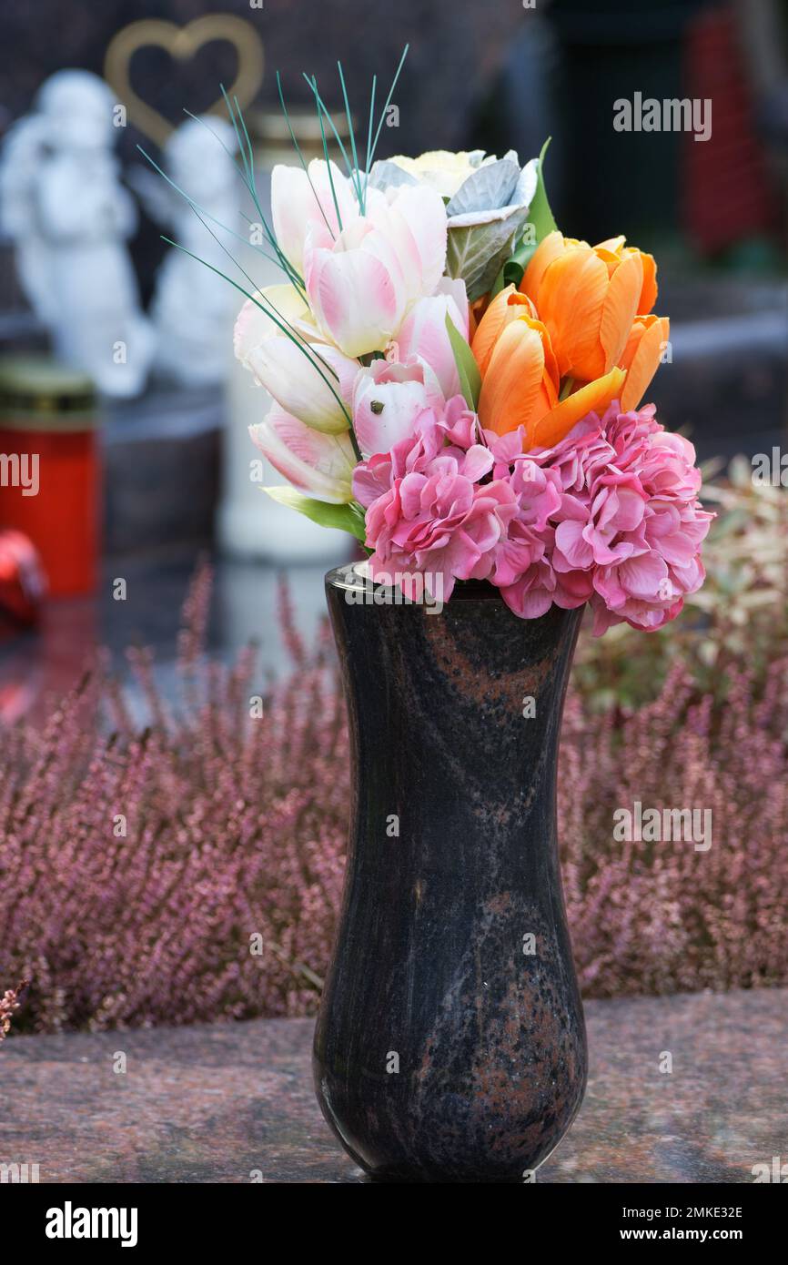 Bunte künstliche Blumen auf einem Grab vor verschwommenem Hintergrund Stockfoto