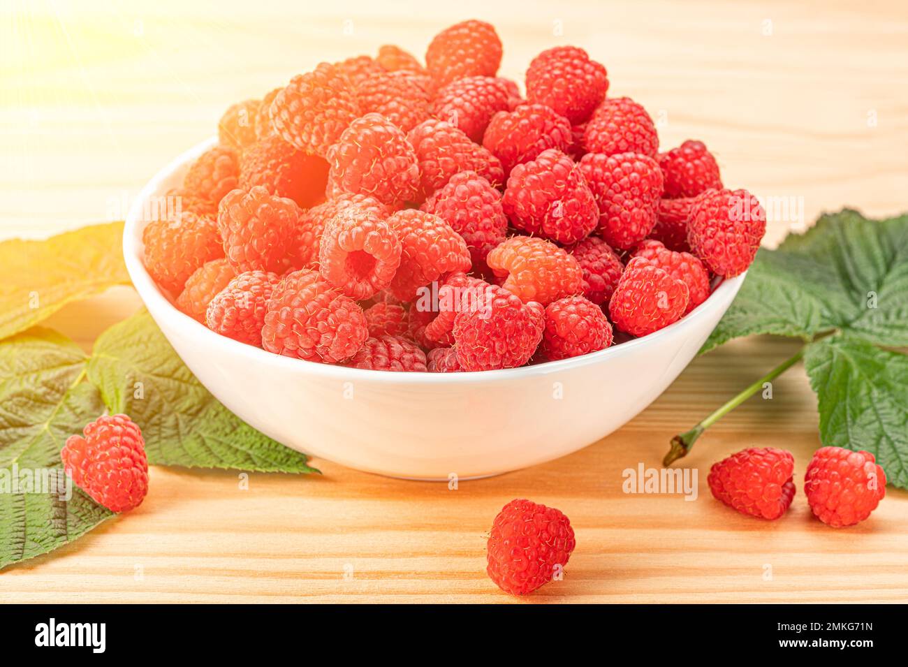 Himbeere auf weißem Teller auf Holztisch an sonnigen Tagen. Teller mit reifen roten Himbeeren stehen auf einem Holztisch vor einem unscharfen grünen Hintergrund. Stockfoto