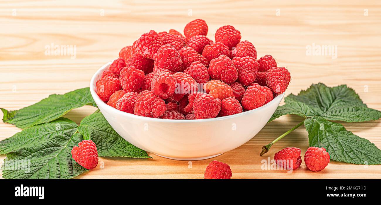 Himbeeren auf weißem Teller auf Holztisch mit Blättern. Bio-Himbeeren ohne den Einsatz von chemischen Düngemitteln und Pestiziden angebaut. Himbeerfrüchte Stockfoto