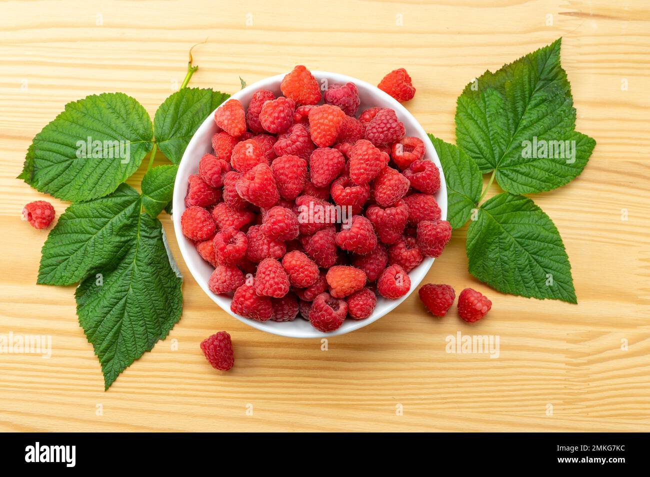 Himbeeren auf weißem Teller auf Holztisch mit Blättern. Bio-Himbeeren ohne den Einsatz von chemischen Düngemitteln und Pestiziden angebaut. Himbeerfrüchte Stockfoto