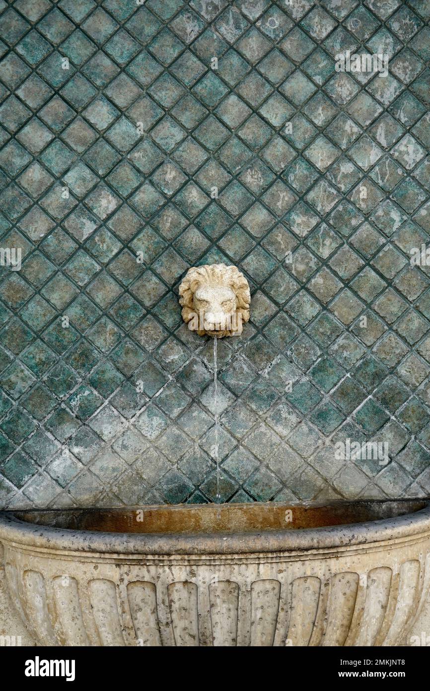 Ein Zementlöwenkopfbrunnen vor einer türkisfarbenen Fliesenwand. Stockfoto
