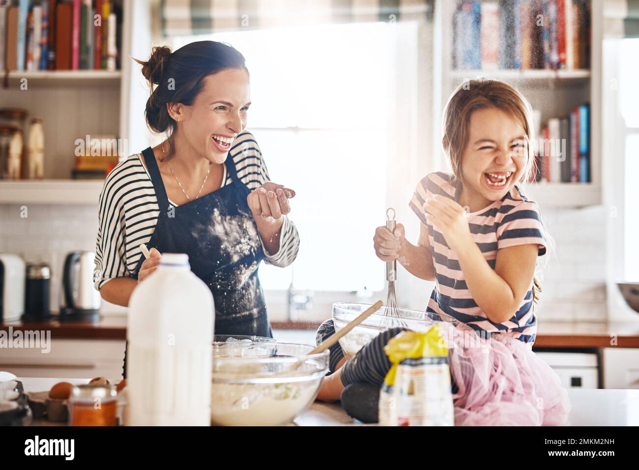 Hier kommt ein Streu von magischem Mehlstaub. Ein kleines Mädchen, das Spaß beim Backen mit ihrer Mutter in der Küche hat. Stockfoto