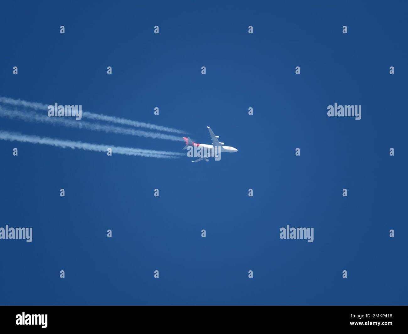 Blick auf ein Flugzeug mit rot-weißer Lackierung, das in großer Höhe mit Kondensstreifen fliegt Stockfoto