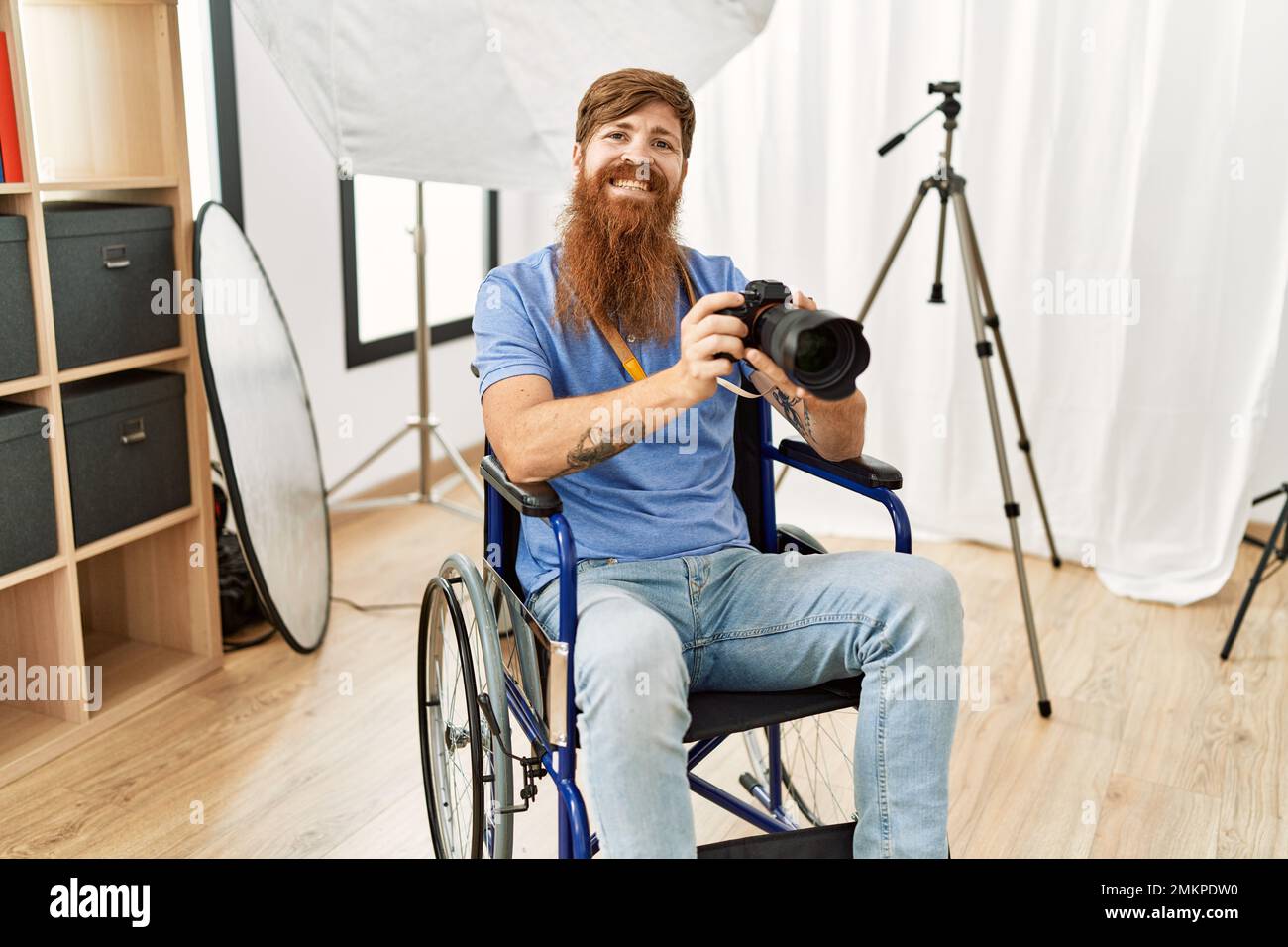 Junger Rotschopf-Fotograf, der in der Klinik mit einer professionellen Kamera auf dem Rollstuhl sitzt Stockfoto