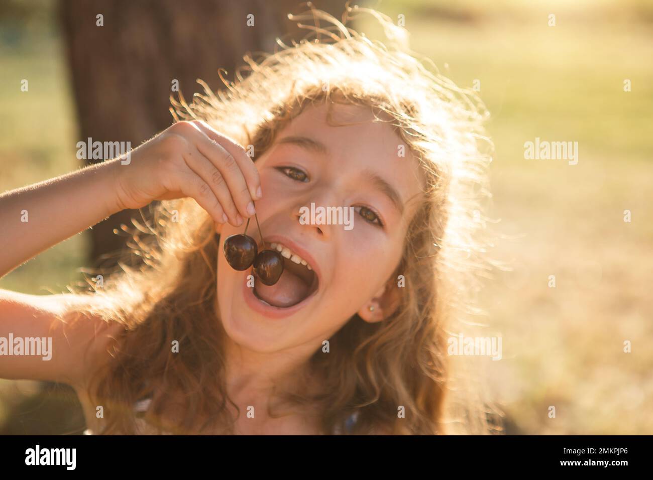 Ein fröhliches, süßes Mädchen mit Kirschbeeren im Mund. Lustiges Sommerporträt eines Kindes mit Kirsche, Geschenke des Sommers, Sommerzeit. Stockfoto