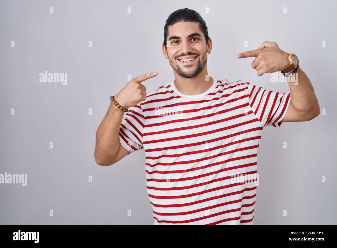 Lateinamerikanischer Mann mit langen Haaren, der über einem isolierten Hintergrund steht und fröhlich mit Fingern, Zähnen und Mund zeigt. Zahngesundheitskonzept Stockfoto