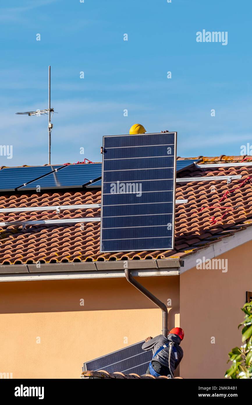 Zwei Techniker, spezialisiert auf Photovoltaikanlagen, arbeiten auf einem Dach, um Solarpaneele zu installieren Stockfoto