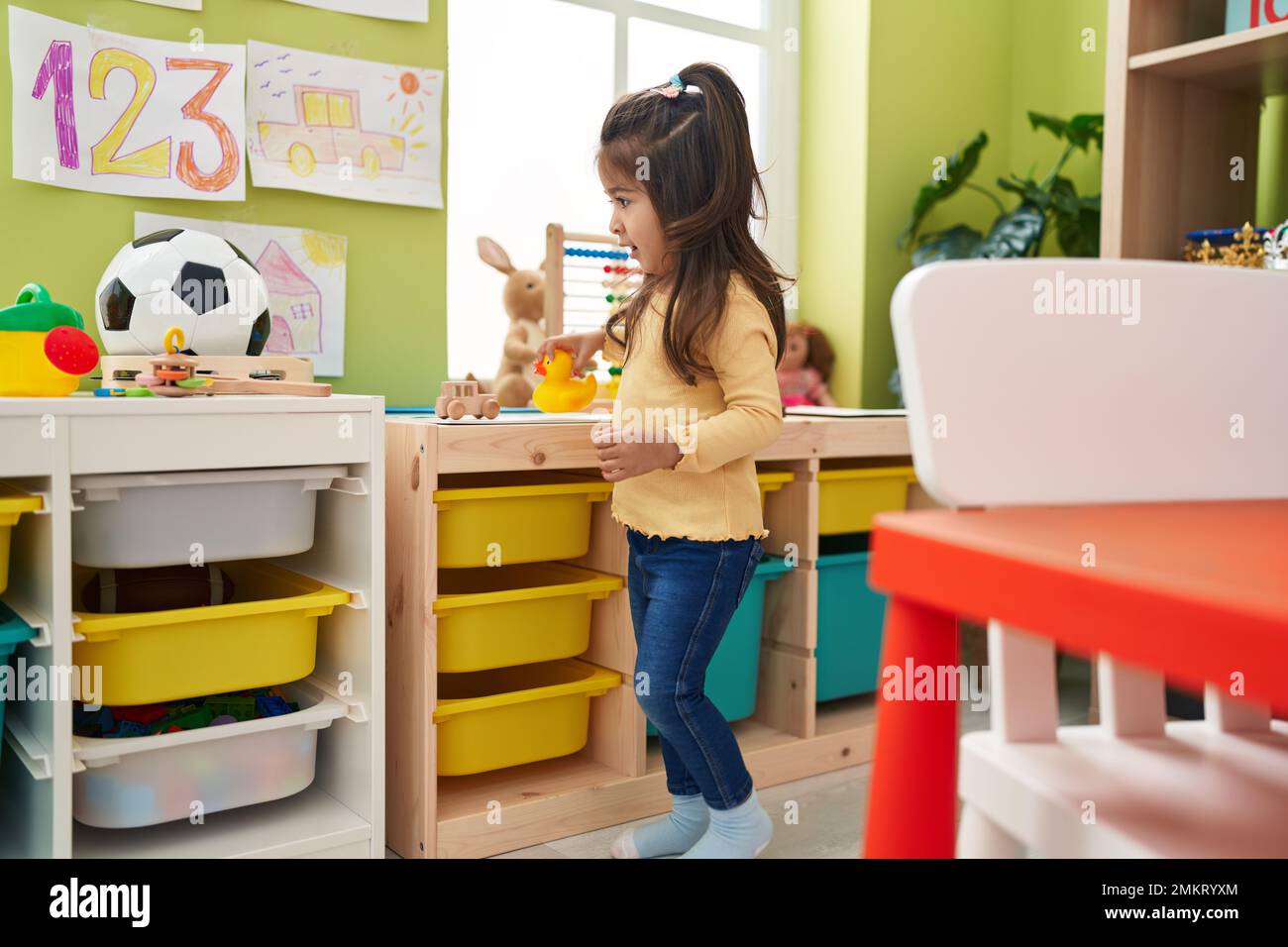 Bezauberndes spanisches Mädchen, das selbstbewusst im Kindergarten mit Entenspielzeug spielt Stockfoto