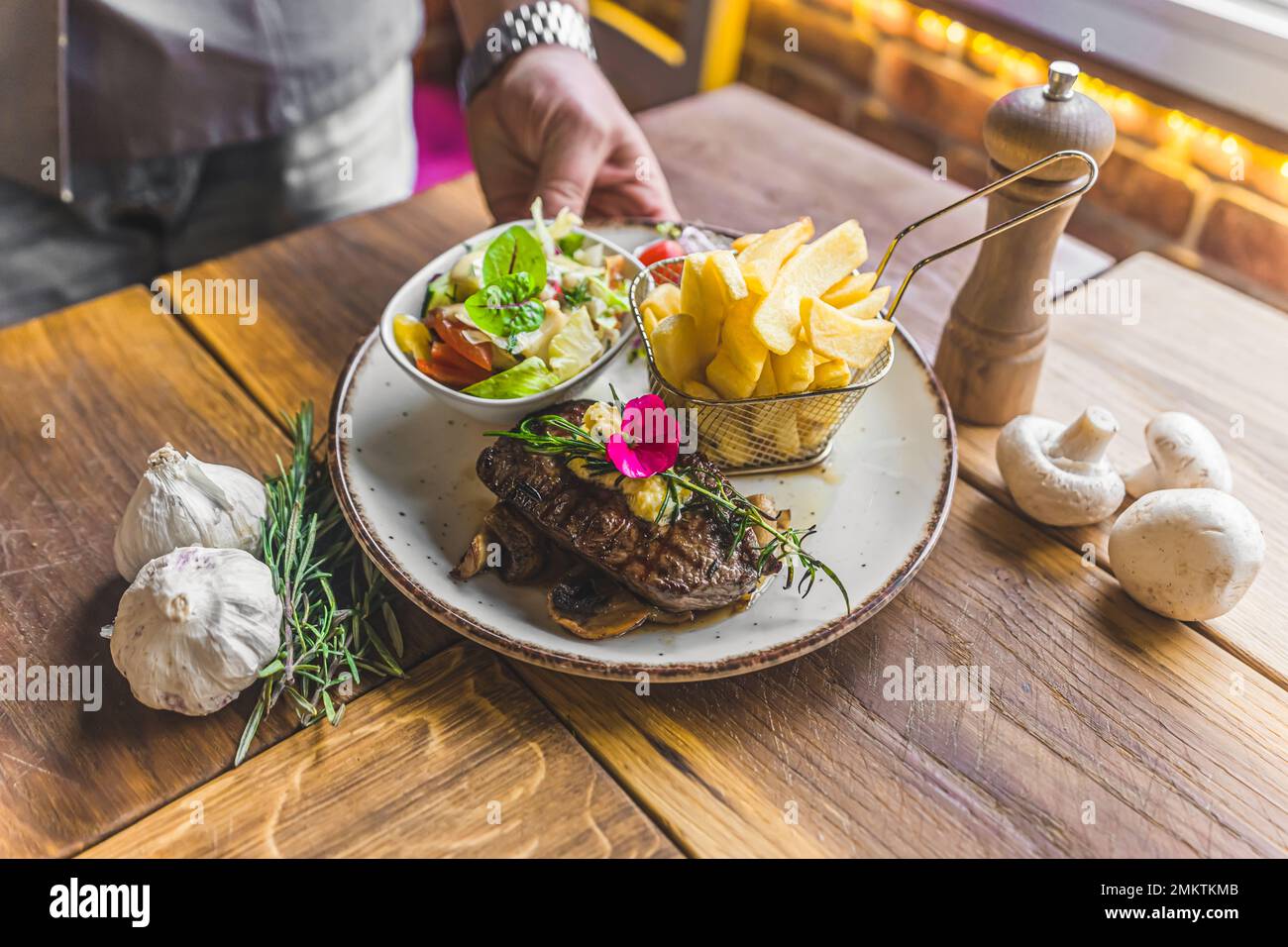 Nicht wiedererkennbare Person, die ein Rinderrührel-Steak mit Pommes Frites und Salat auf weißem Teller serviert. Essen im Restaurant. Horizontale Indoor-Aufnahme. Hochwertiges Foto Stockfoto