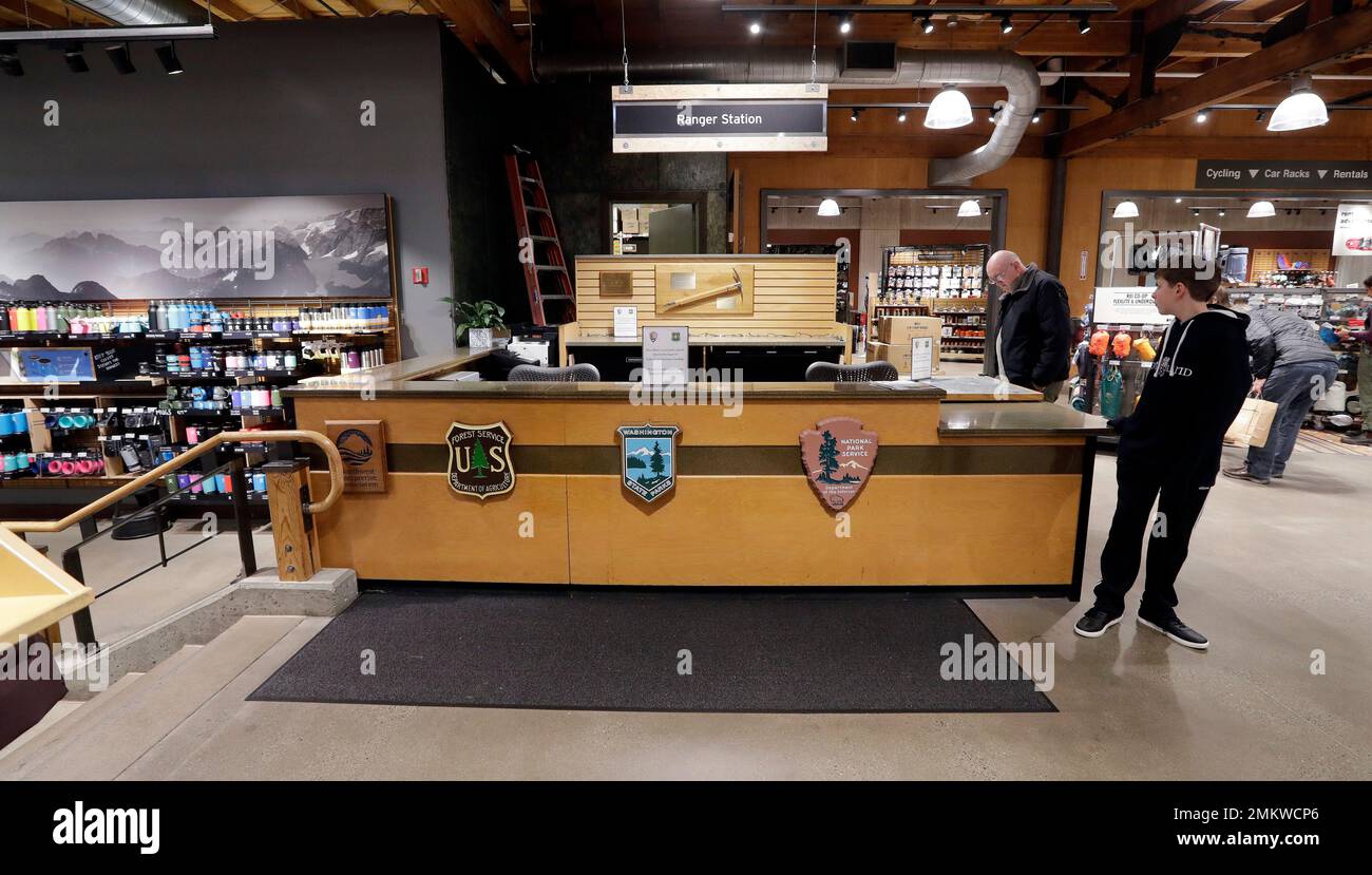REI Co-op customers stand near an unstaffed ranger station kiosk, closed as part of the federal government shutdown, inside the flagship store Wednesday, Dec. 26, 2018, in Seattle. The desk is normally staffed by rangers who provide recreational information and passes for public lands in Washington state as part of a partnership with the National Park Service, US Forest Service, Washington State Parks, and REI. The shutdown started Saturday when funding lapsed for nine Cabinet-level departments and dozens of agencies. (AP Photo/Elaine Thompson) Stockfoto
