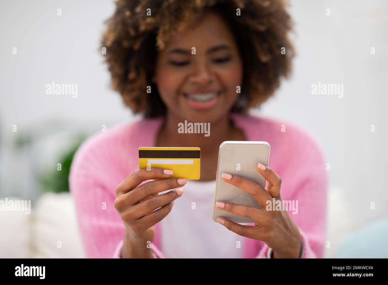 Glückliche, hübsche, schwarze Dame, die auf der Couch sitzt und online bestellt Stockfoto