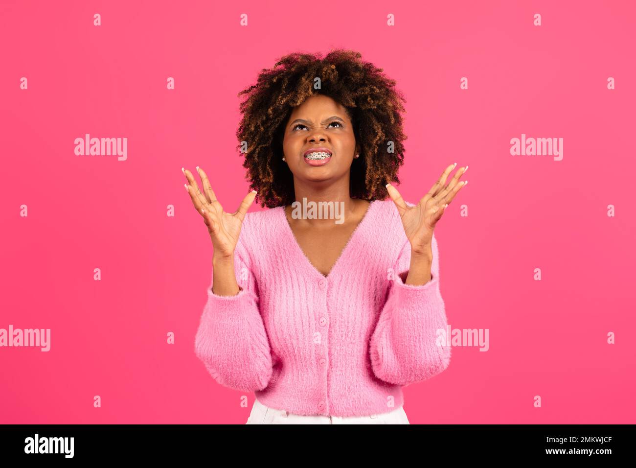 Wütend aufgeregte junge schwarze lockige Frau, die sich in lässiger Klammer die Hände hebt und nach oben schaut Stockfoto