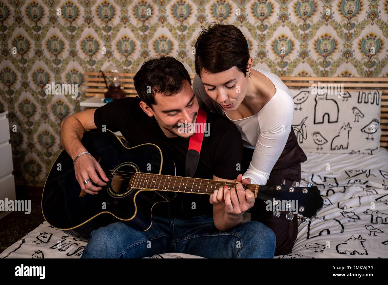 Der junge Mann bringt seiner Freundin Gitarre bei. Ein Paar Leben und ein lustiges Konzept. Stockfoto