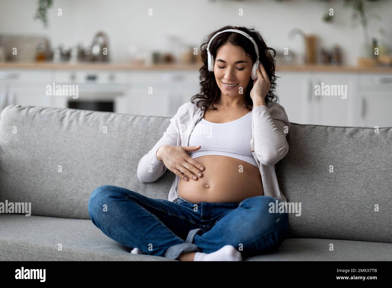 Schöne Schwangere, Die Musik Mit Kabellosen Kopfhörern Hört, Während Sie Sich Auf Dem Sofa Entspannt Stockfoto