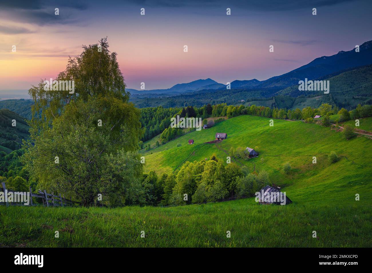 Holzhütten auf den grünen Hängen bei Sonnenuntergang. Atemberaubende ländliche Sommerlandschaft, Siebenbürgen, Rumänien, Europa Stockfoto