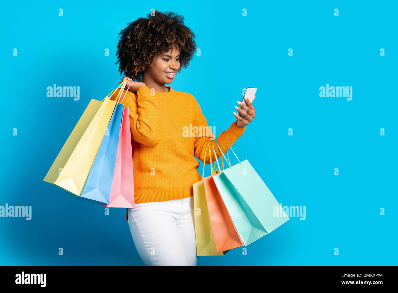Positive afrikanische Frau, die online einkauft, Smartphone auf Blau benutzt Stockfoto