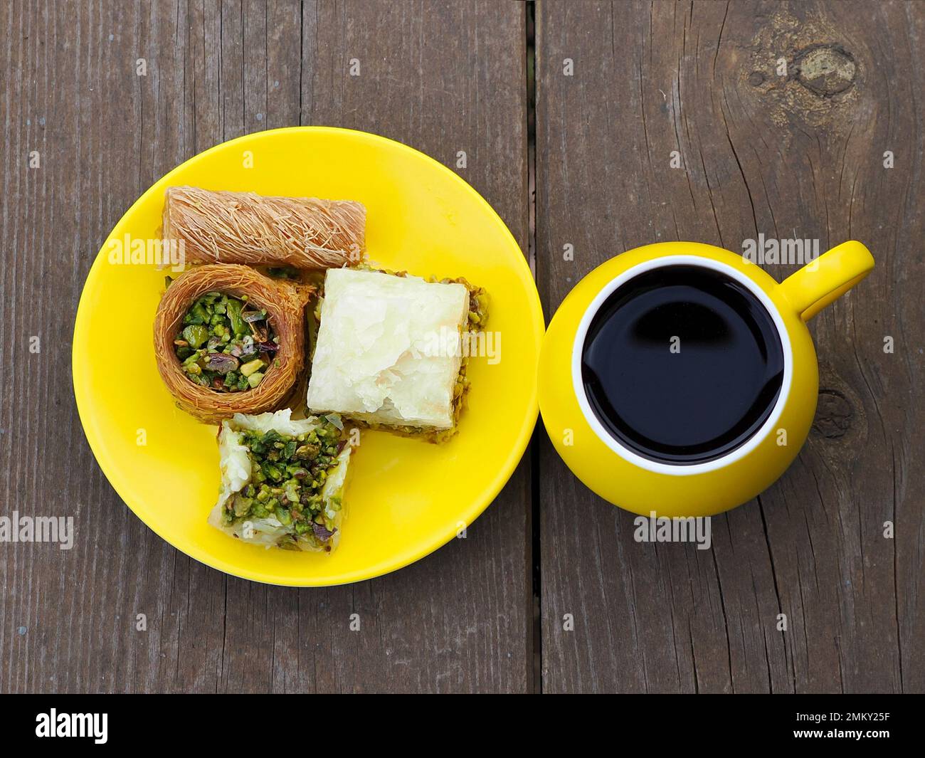 Kadaif und Baklava auf einer gelben Untertasse und Morgenkaffee. Holzhintergrund. Stockfoto