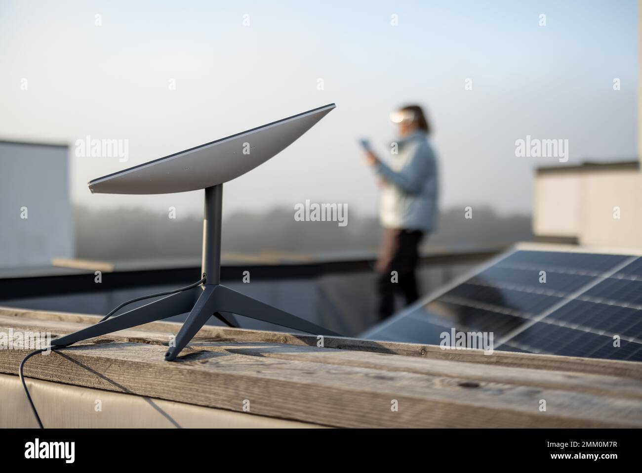 Starlink-Satellitenschüssel auf dem Dach des Wohngebäudes und Frau im Hintergrund Stockfoto