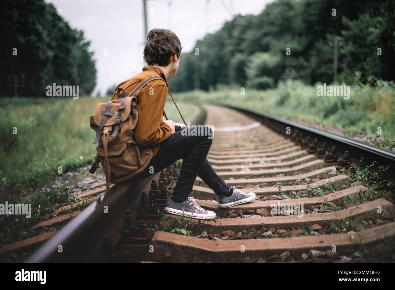 Fotograf in brauner Jacke mit Rucksack und Retro-Kamera auf der Eisenbahn Stockfoto