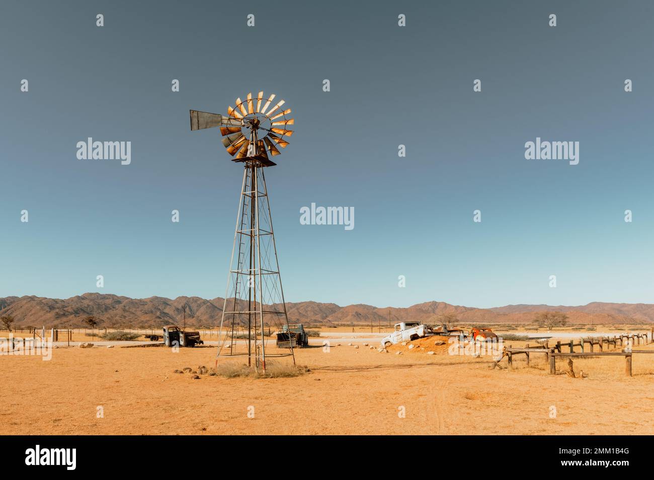 Verlassener, alter Autofriedhof und alte rostige Windturbine in der sandigen Wüste mit blauem Himmel im Hintergrund Stockfoto