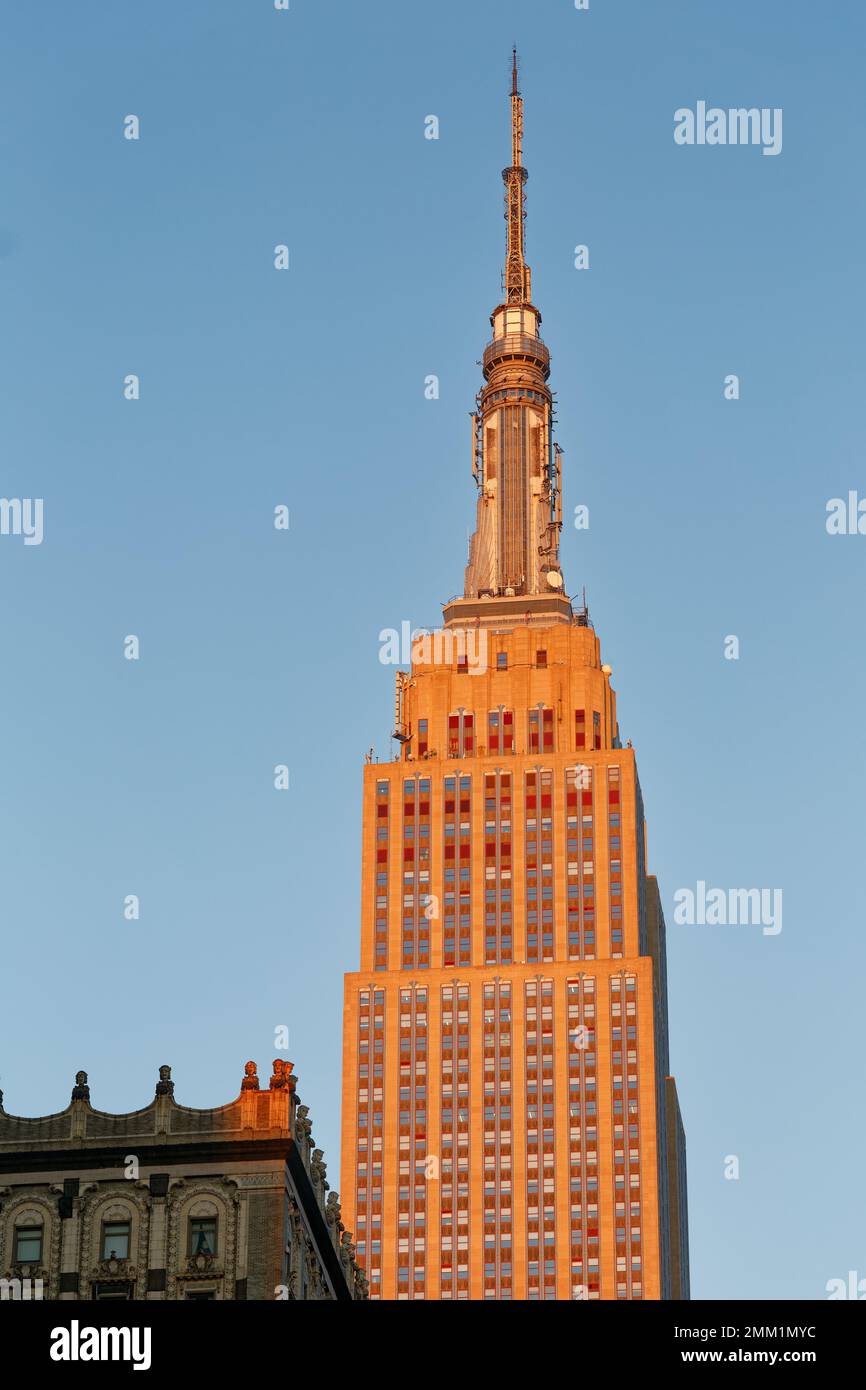 NYC: Die östliche Fassade des Empire State Building verläuft bei Sonnenaufgang von grau bis goldrot, wenn die Sonne am tiefsten Punkt steht. Stockfoto