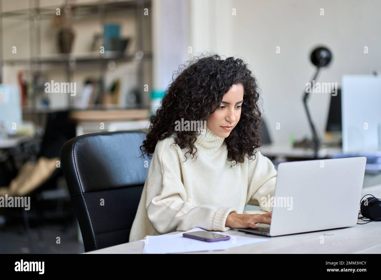 Junge lateinische Geschäftsfrau, die am Schreibtisch sitzt und an einem Laptop arbeitet. Stockfoto