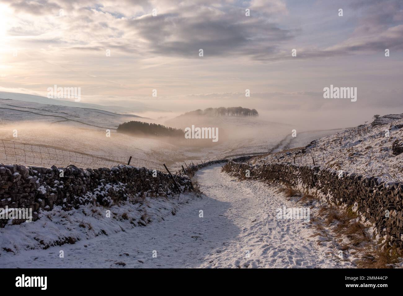Der von Mauern umgebene Pfad nach Horton-in-Ribblesdale führt vom Berg Pen-y-ghent an einem verschneiten Wintertag mit leichtem Nebel und Sonnenschein in der Yorkshire Da hinab Stockfoto