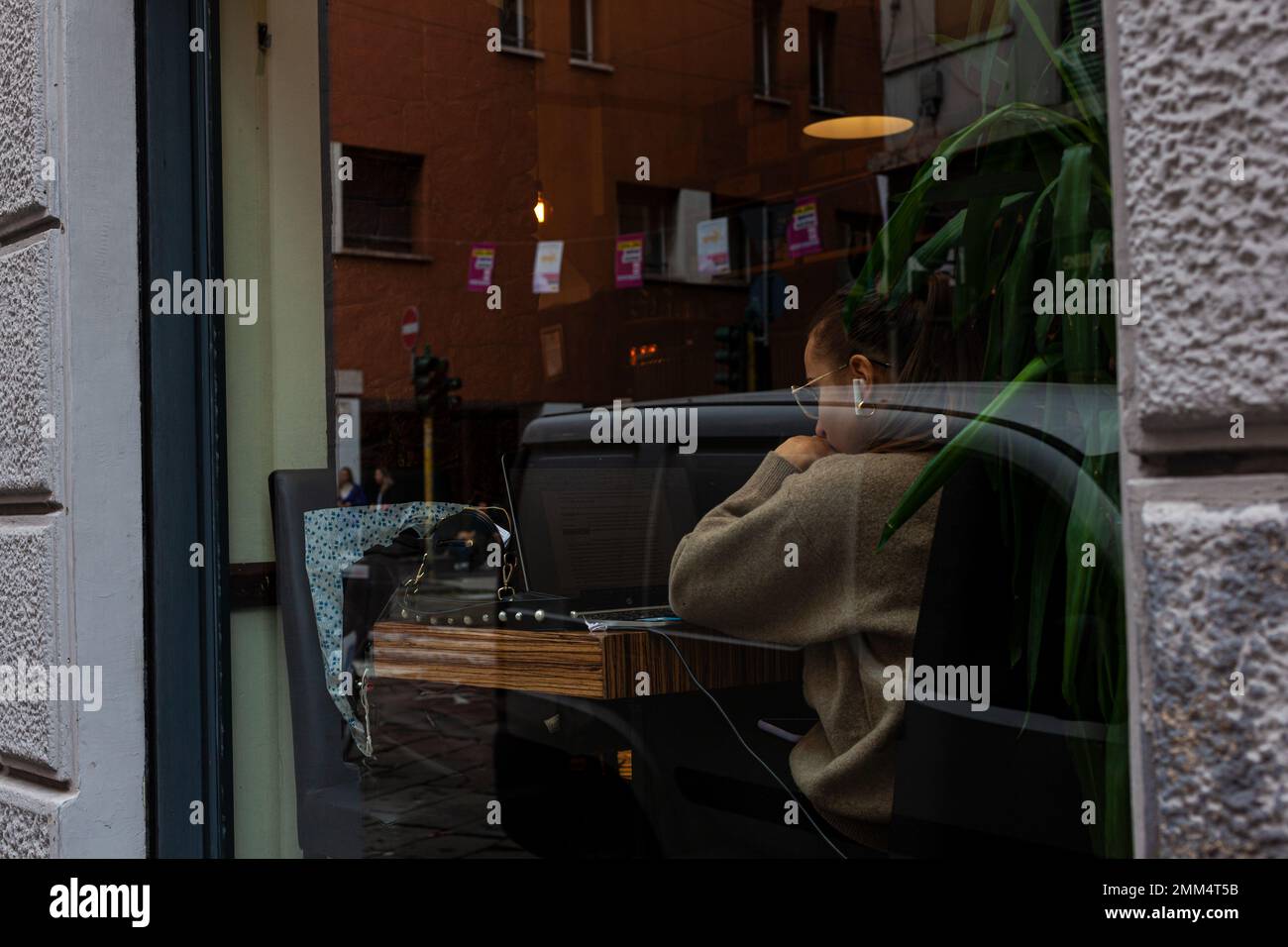 Mailand, Italien - Ottobre 16, 2022: Blick durch das Fenster einer jungen Frau, die ihren Laptop in der Cafeteria benutzt Stockfoto