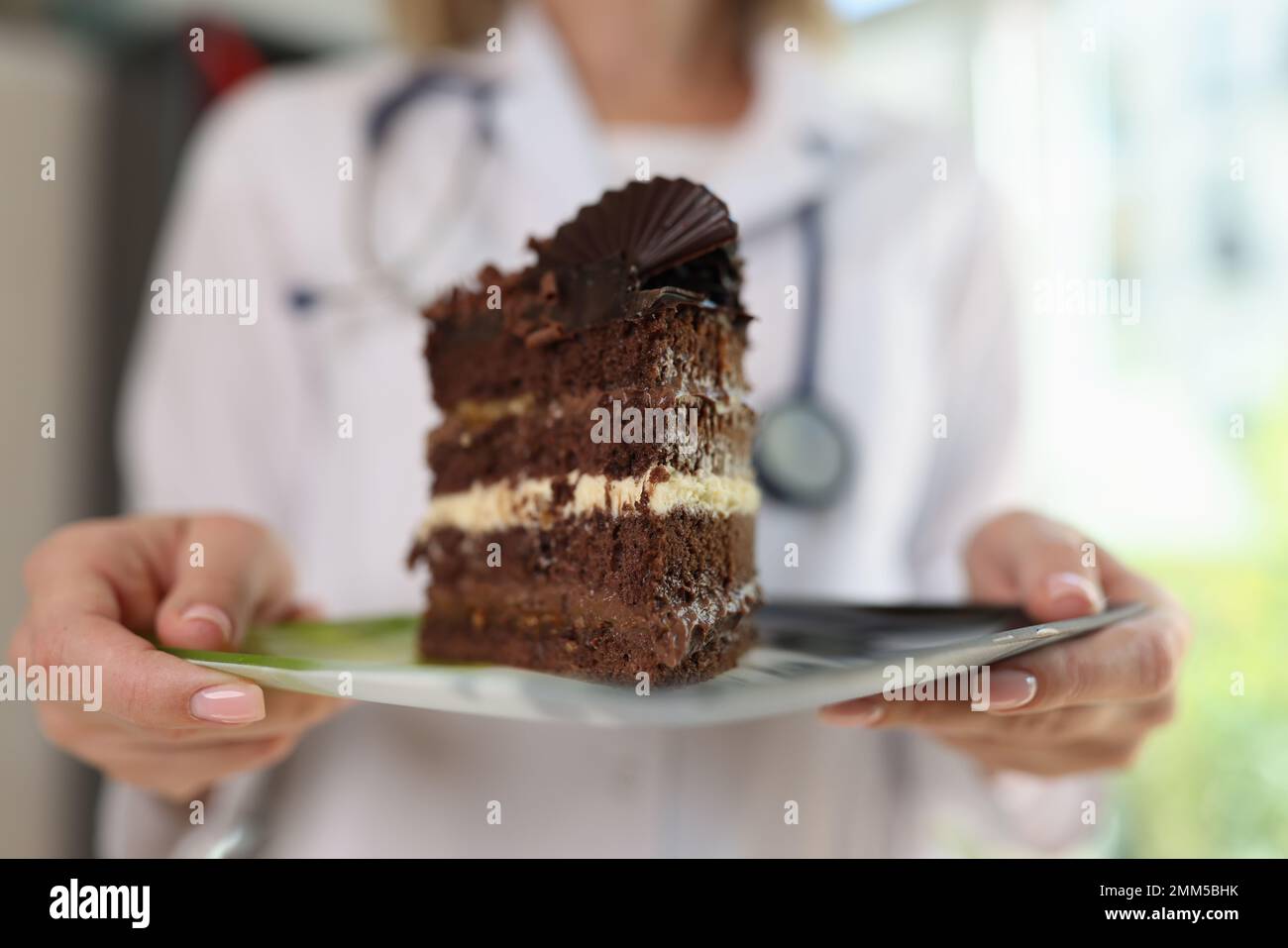 Eine Ärztin mit Stethoskop hält Schokoladenkuchen auf dem Teller in ihren Händen. Stockfoto