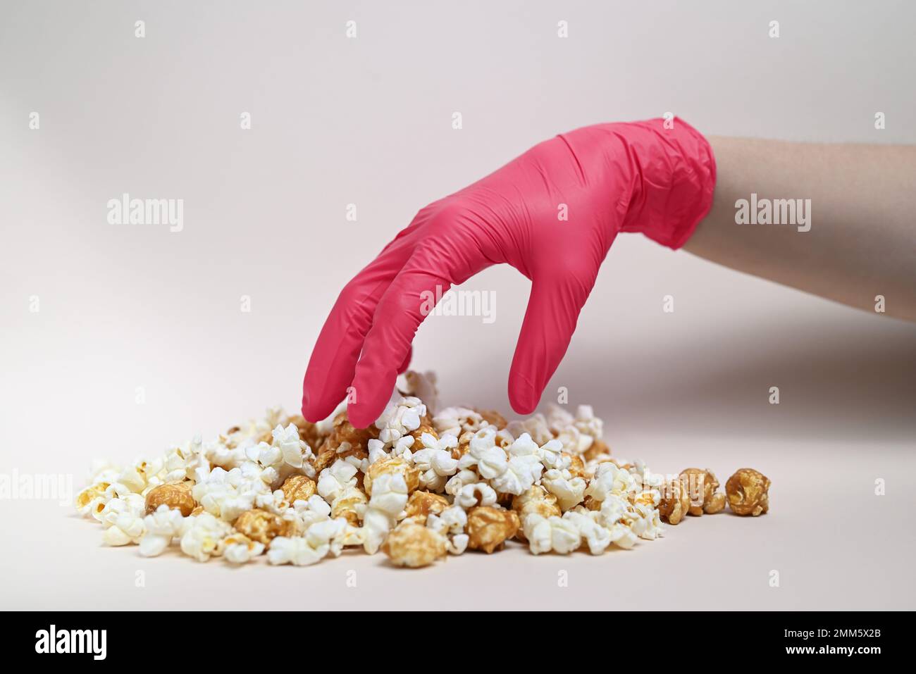 Abstrakte Zusammensetzung. Eine Hand in einem Viva Magenta-farbenen Handschuh greift nach Popcorn. Popcorn-Mix, Karamell und gesalzenes Popcorn. Stockfoto