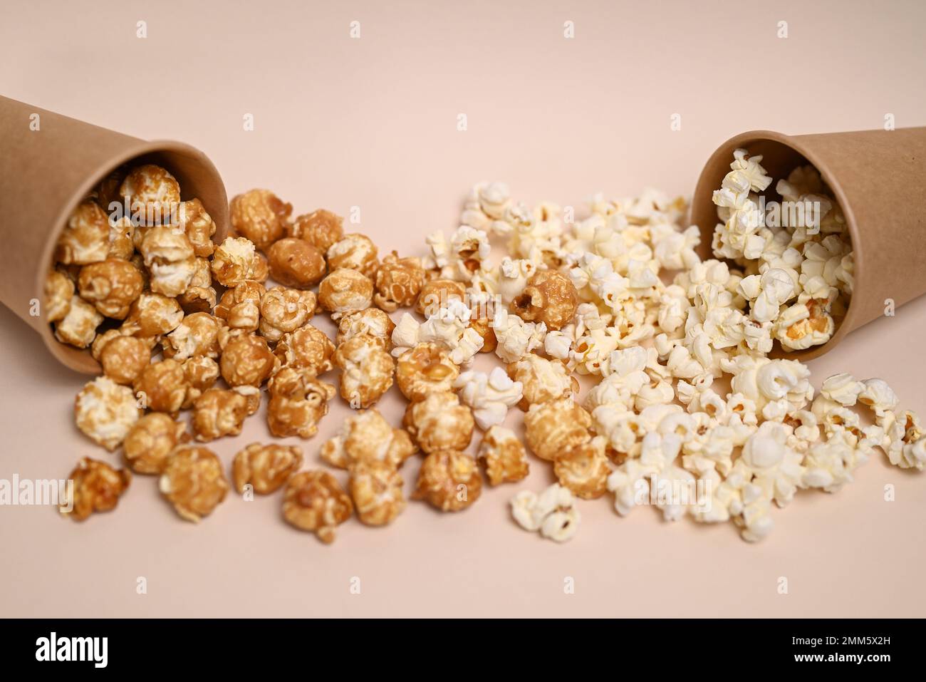 Zwei Arten Popcorn in zwei Pappbechern. Сaramel-gedecktes und gesalzenes Popcorn. Popcorn verschüttete aus den Tassen und mischte sich. Geringe Schärfentiefe. Stockfoto