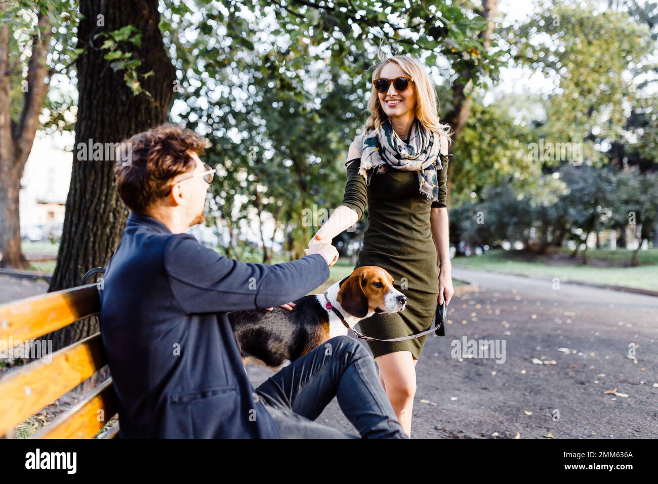Ein Mann mit einem Beagle begrüßt eine junge Blondine im Park Stockfoto